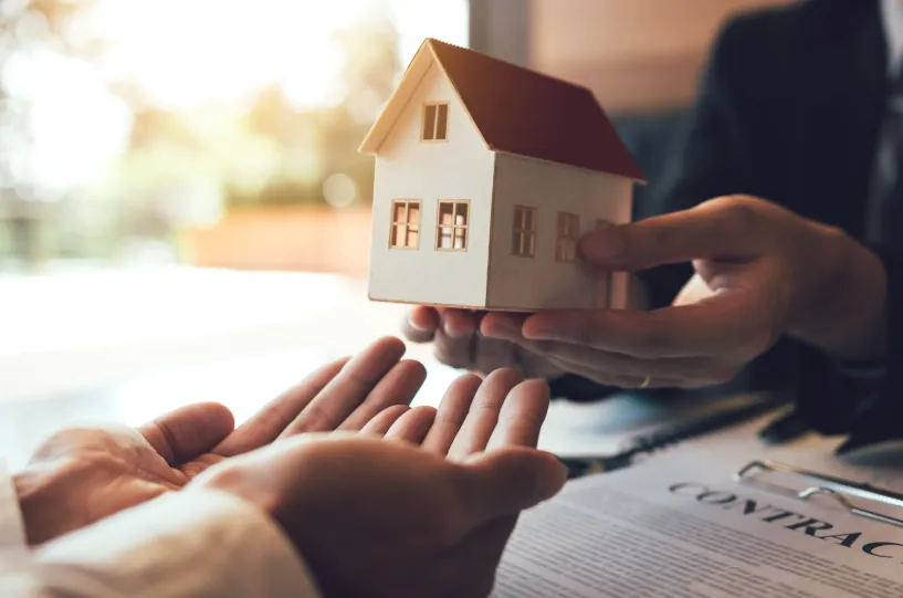 A real estate transaction with a person handing over a small house model, symbolizing home leasing and decisions around how much rent can i afford.