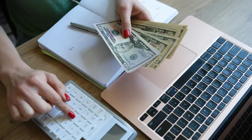 A person calculating finances with cash, a calculator, and a laptop, illustrating the importance of budgeting for rent and the pet fee.