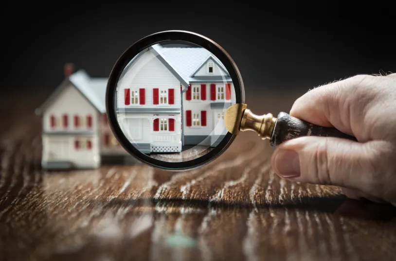 A magnifying glass focusing on a model home, representing the detailed property search process in "what is an apartment locator" services.