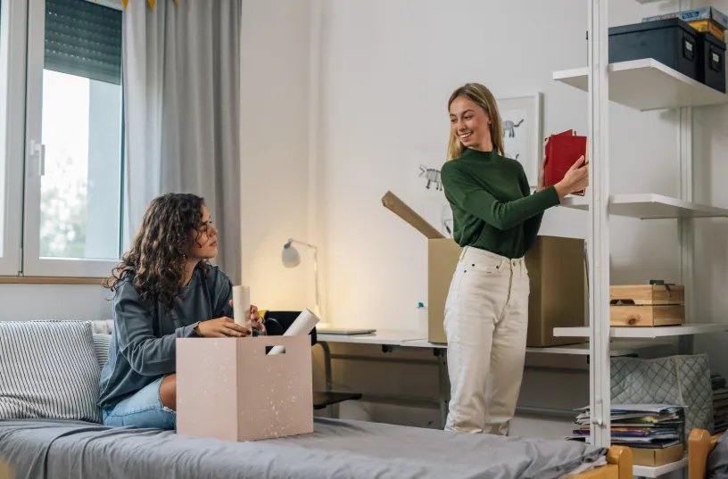Two young women unpacking in a shared apartment, highlighting the benefits of having roommates as a way of how to save money on rent.