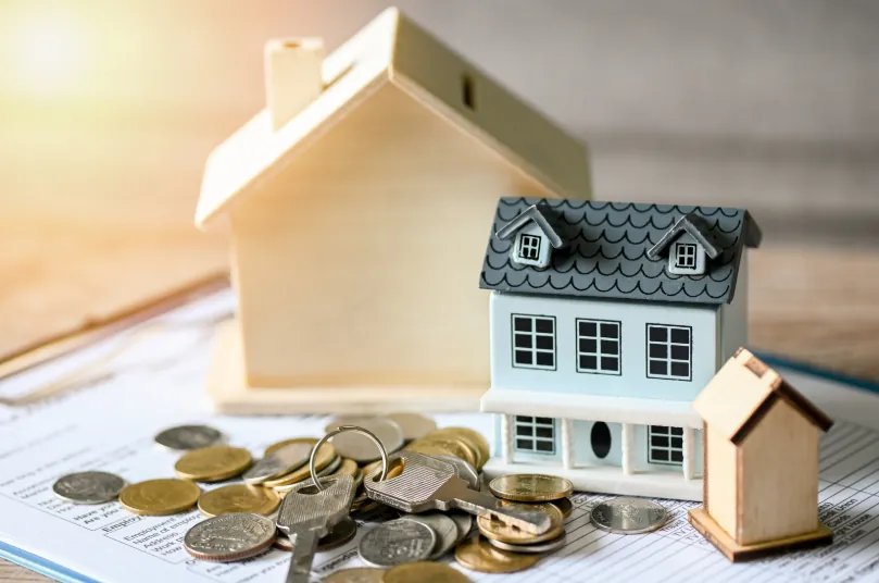 Small house models, coins, and keys on financial documents, illustrating budgeting and deposit strategies for how to get an apartment with bad credit.