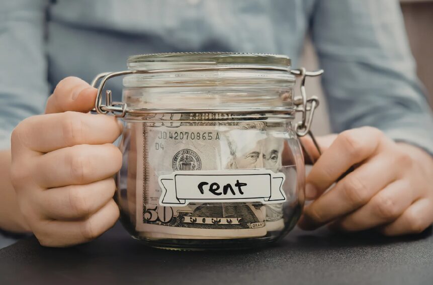 A person holding a glass jar filled with cash and a label that says "rent"