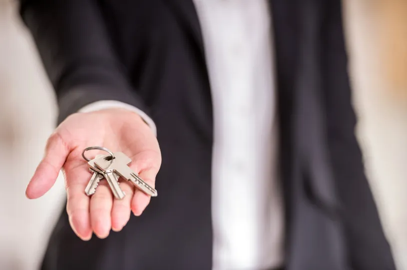 A real estate agent extending house keys, symbolizing negotiation tactics and lease agreements that impact how to save money on rent.