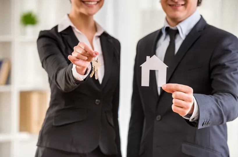 Two real estate agents in suits holding house keys and a paper house cutout, emphasizing rental agreements and additional costs like the pet fee.